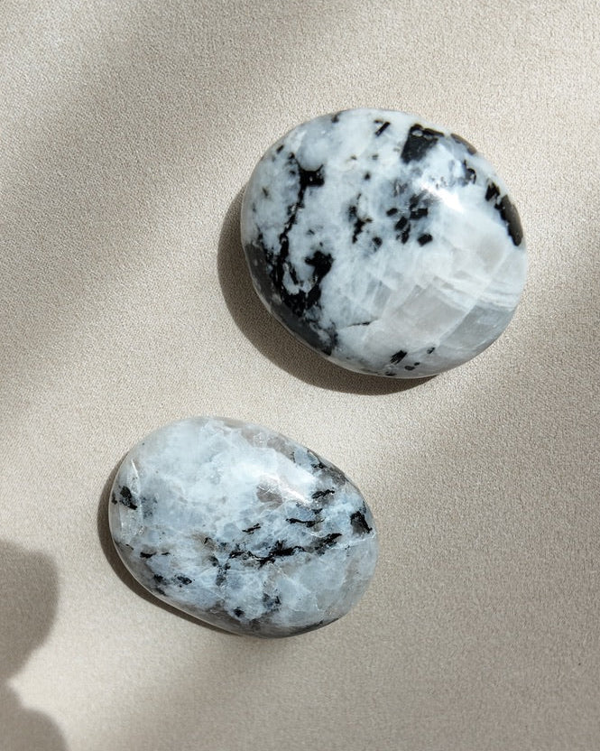 Two polished black-and-white marbled stone pendants displayed on a neutral beige textured surface with soft shadows.