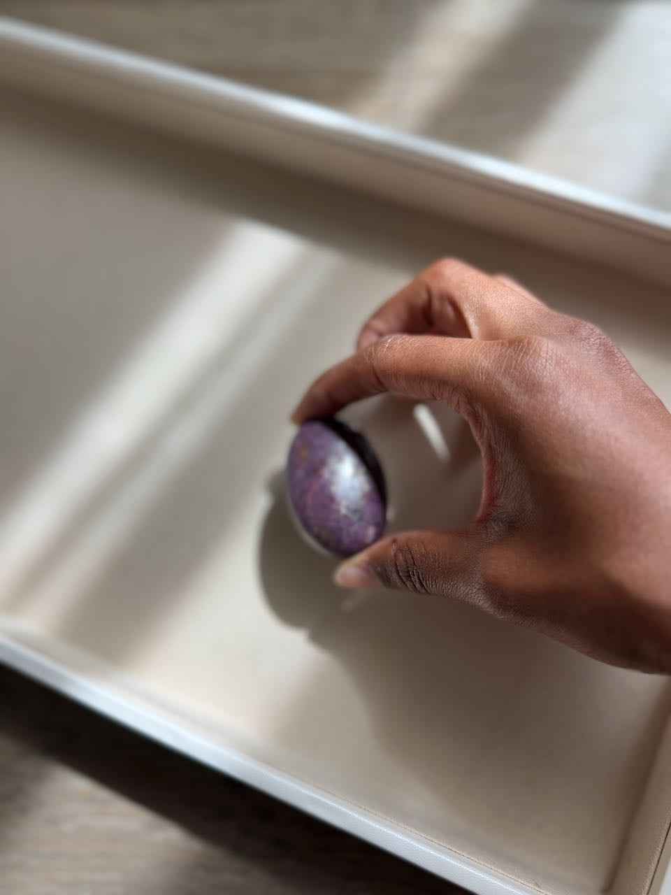 A lilac phosphosiderite palm stone held between two fingers