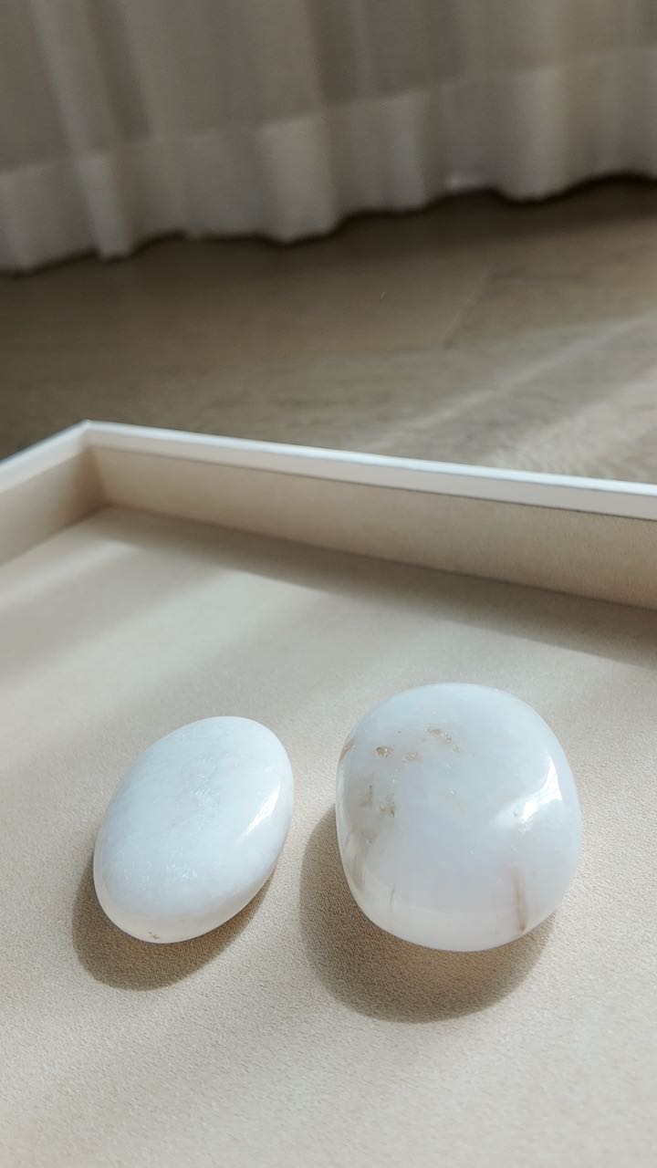 The pair of scolecite palm stones, one showing a soft rust-toned inclusion